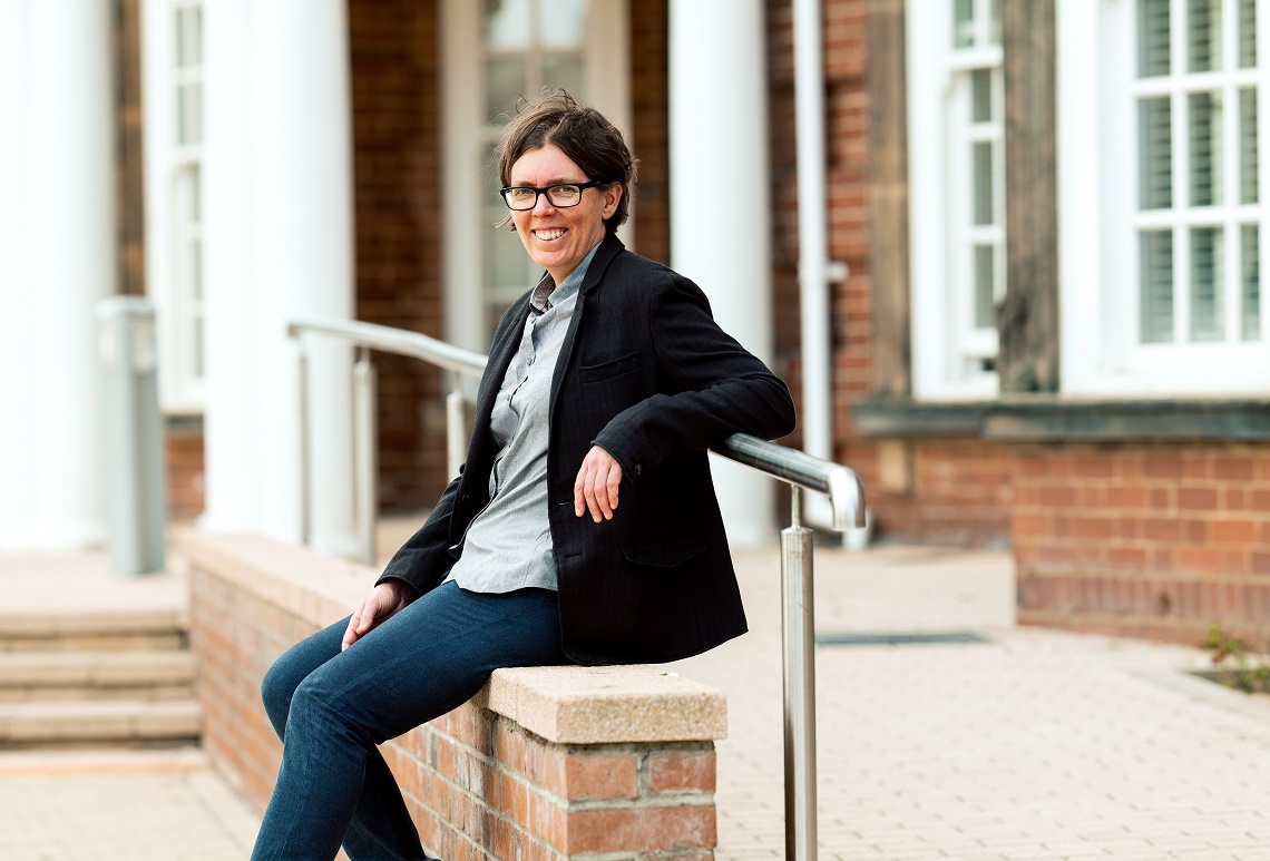 Claire Bambra sitting on a wall smiling at the camera